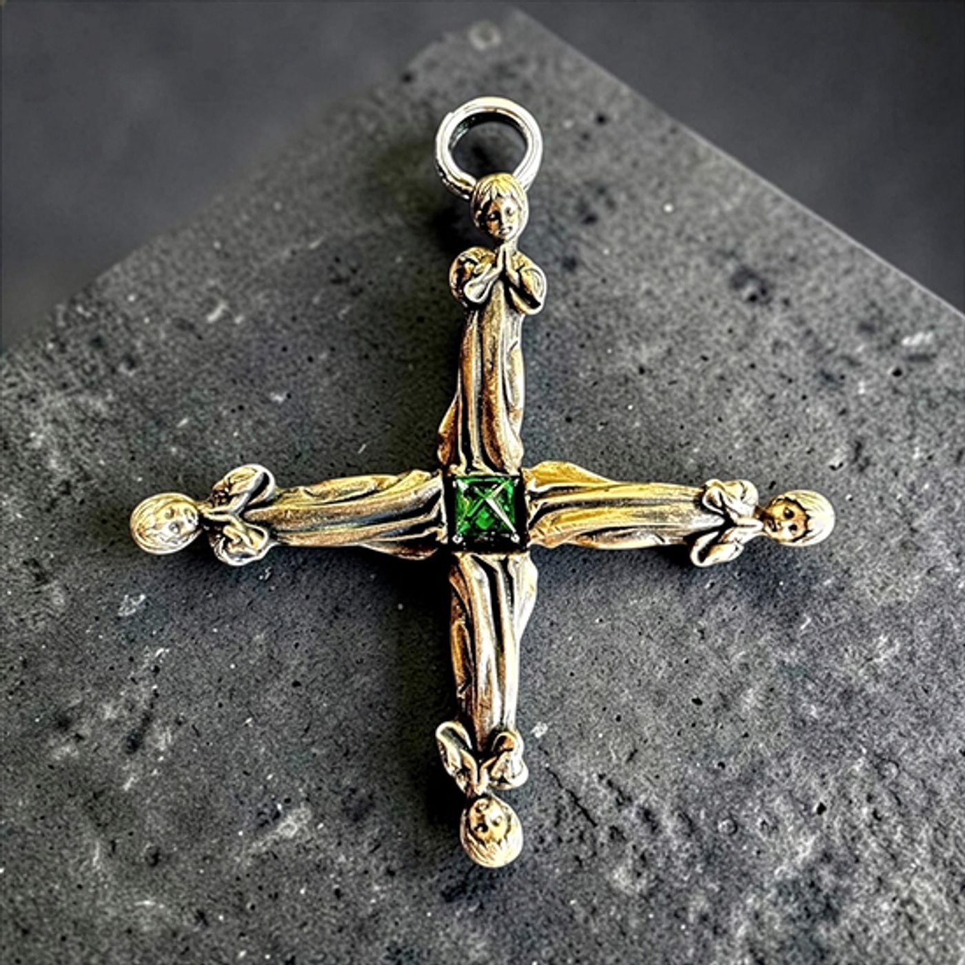 Silver cross by Michelline Syjuco assembled from wingless angel figures around a green center stone