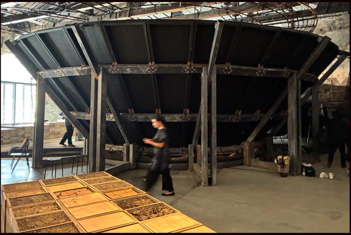 A visitor walks past the vast tilted timber structure of the Philippine Pavilion at the Venice Architecture Biennale, soil trays in the foreground
