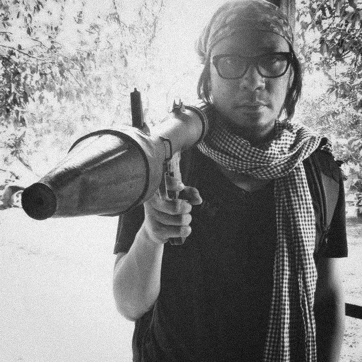 Lourd de Veyra in glasses and a checked scarf, shouldering a rocket launcher, in black and white