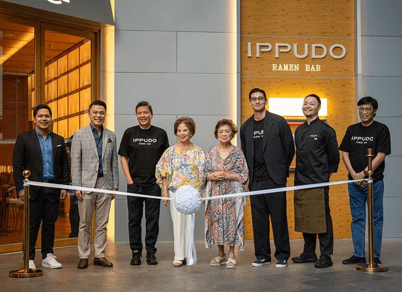 Eight executives and chefs line up for the ribbon cutting beneath the Ippudo Ramen Bar sign