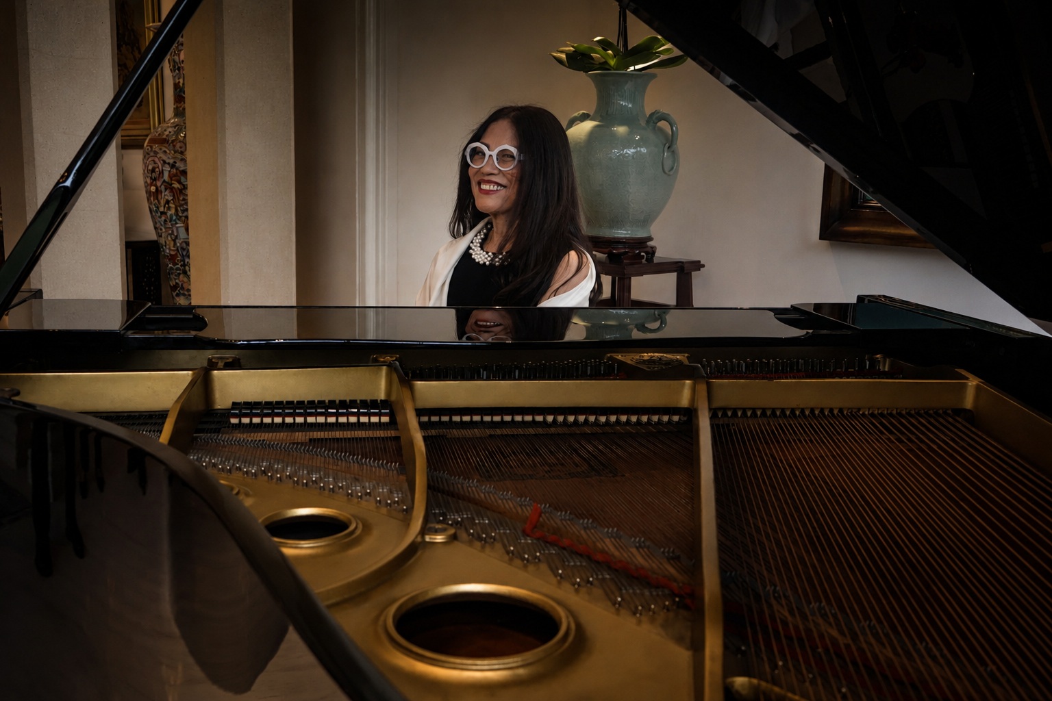Cecile Licad in white-framed glasses smiles from behind an open concert grand piano