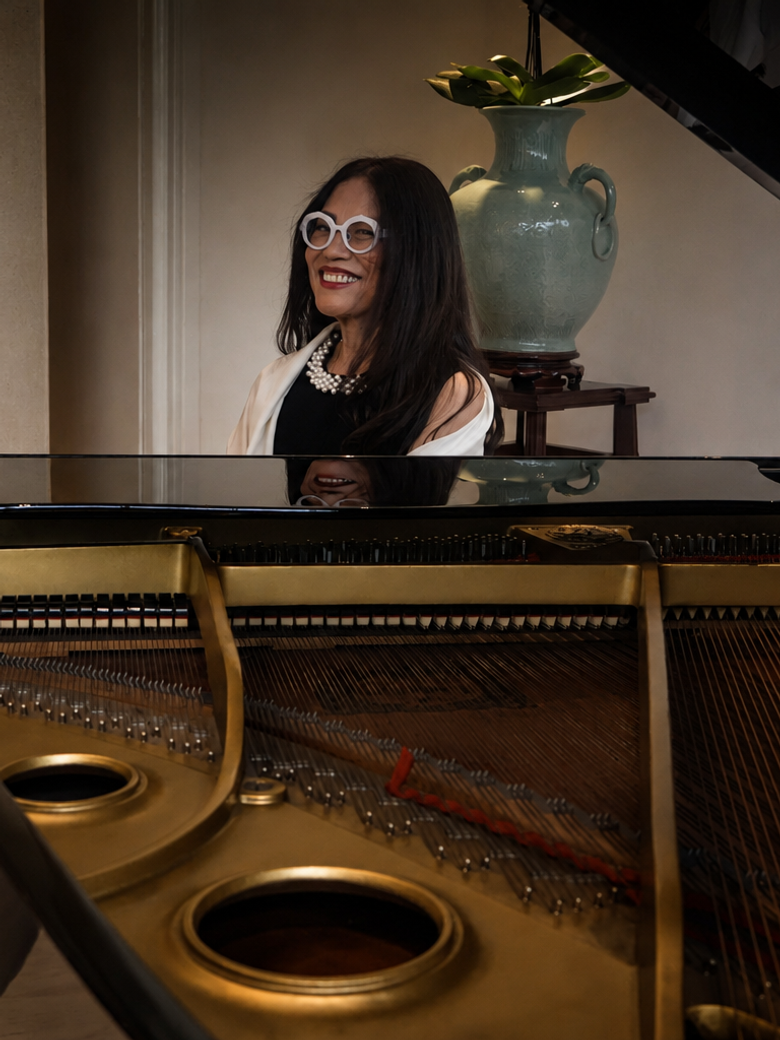 Cecile Licad in white-framed glasses smiles from behind an open concert grand piano
