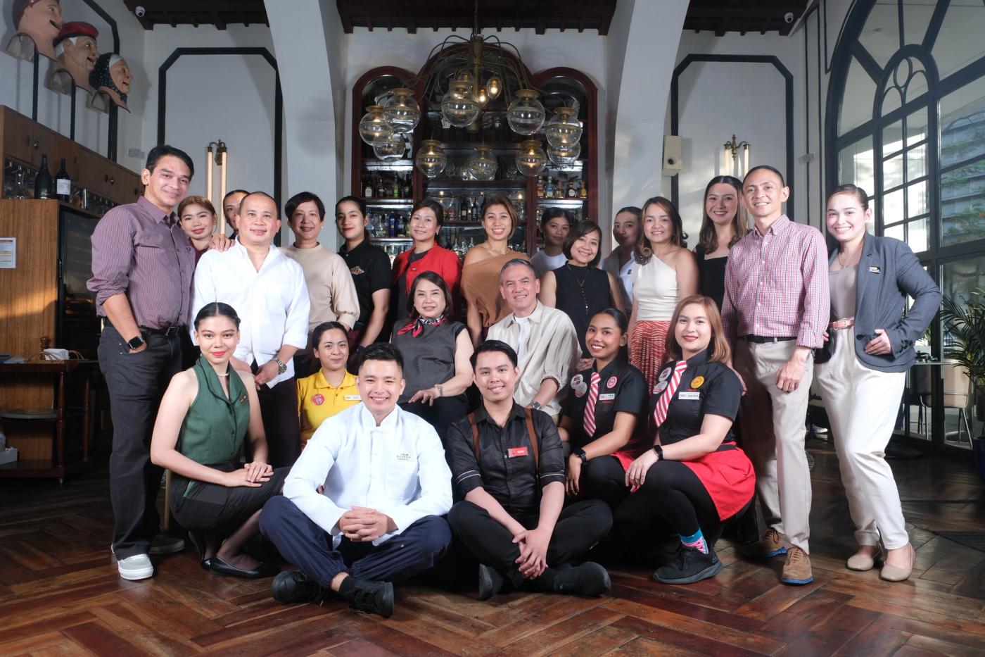 The Bistro Group crew, servers in uniform and managers together, posed for a group portrait in a heritage dining room