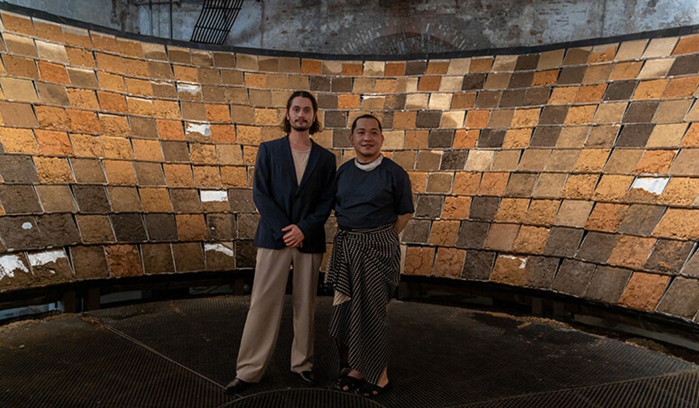 Curator Renan Laru-an and artist Christian Tenefrancia Illi inside a curved wall of earthen bricks