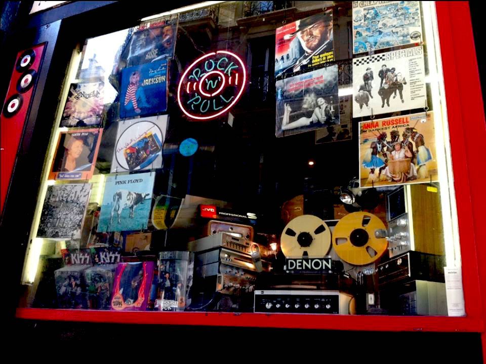 Night shop window packed with LP sleeves around a neon rock ‘n’ roll sign and gold reel-to-reel decks