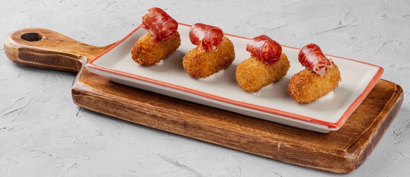 Four golden croquettes draped with curls of Jamon Iberico on a long white plate