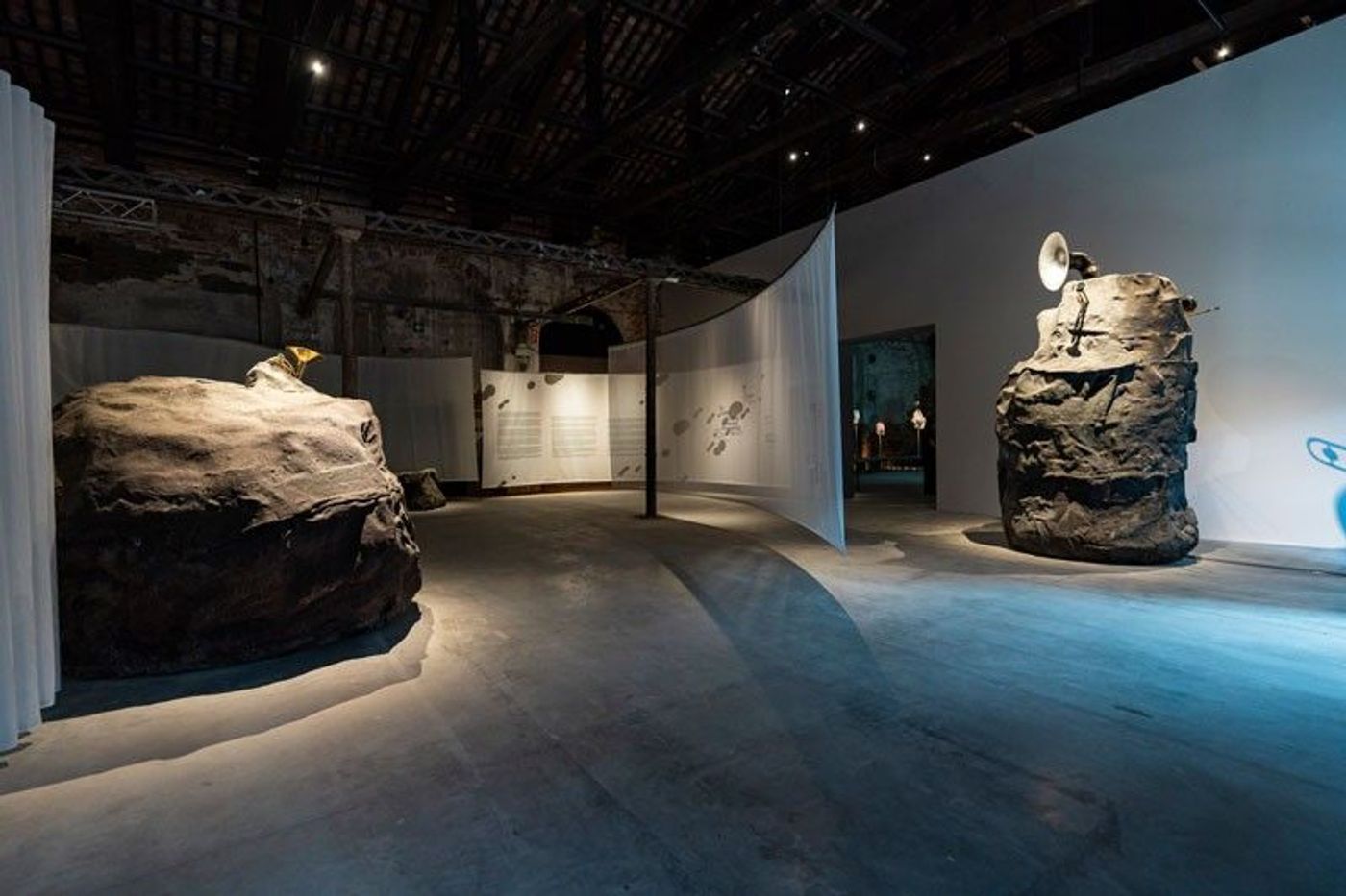 Wide view of the Philippine Pavilion at the Arsenale, with two boulder sculptures and hanging curtains under a timber-beamed brick hall