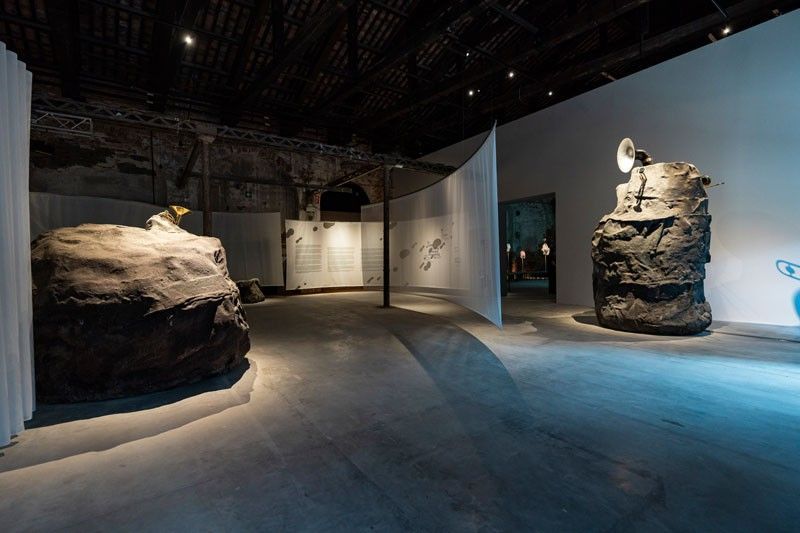 Wide view of the Philippine Pavilion at the Arsenale, with two boulder sculptures and hanging curtains under a timber-beamed brick hall