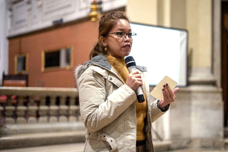 Tessa Maria Guazon speaking into a microphone inside a Venetian church, cue card in hand