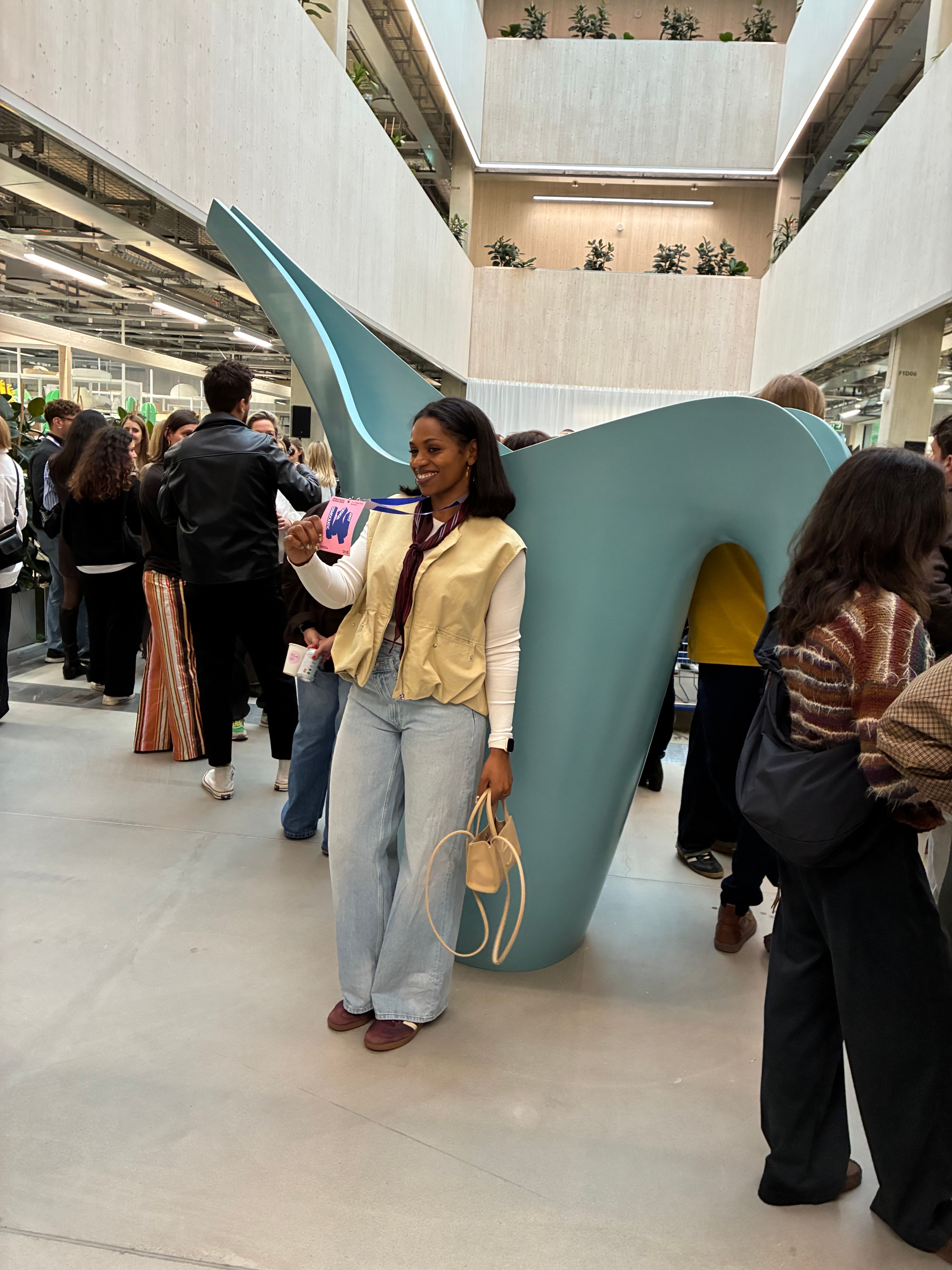 Guest smiling beside a giant pale blue watering can sculpture in a bright atrium during the IKEA event in Älmhult