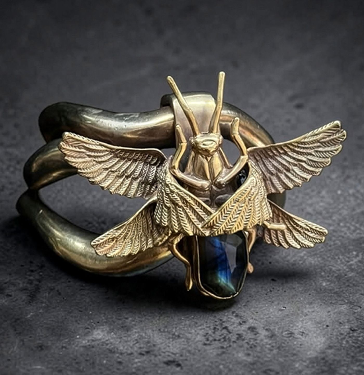 Gold cuff by Michelline Syjuco topped with a winged roach built from cannibalized parts over a labradorite stone
