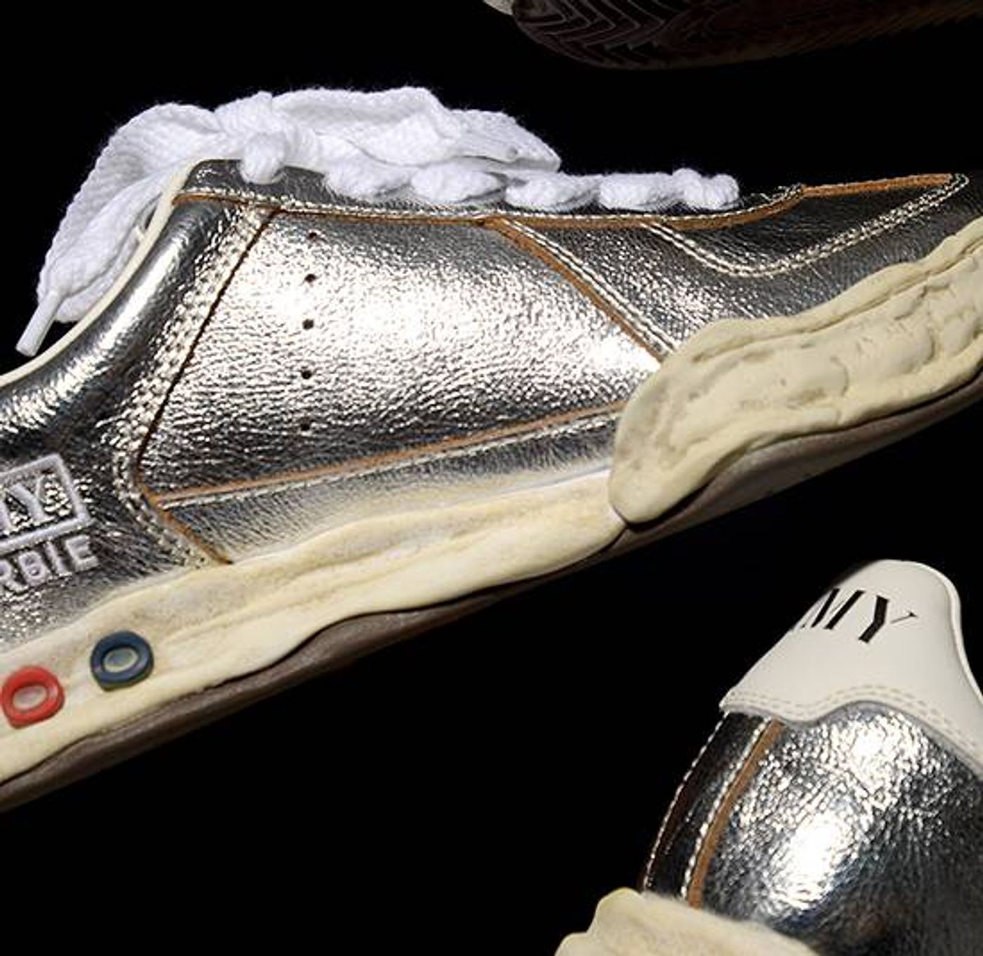 A pair of shiny metallic silver Maison Mihara Yasuhiro Blakey low-top sneakers showing deconstructed wavy rubber soles