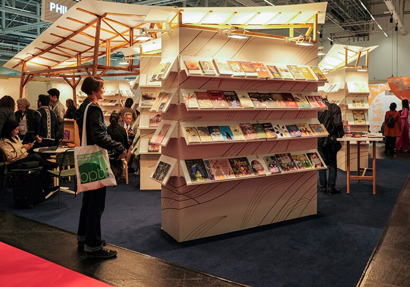 The Philippine National Stand at the Buchmesse: fins of books on white shelving rising from a rattan-skinned kiosk beneath kite-like canopies, browsers leafing through titles