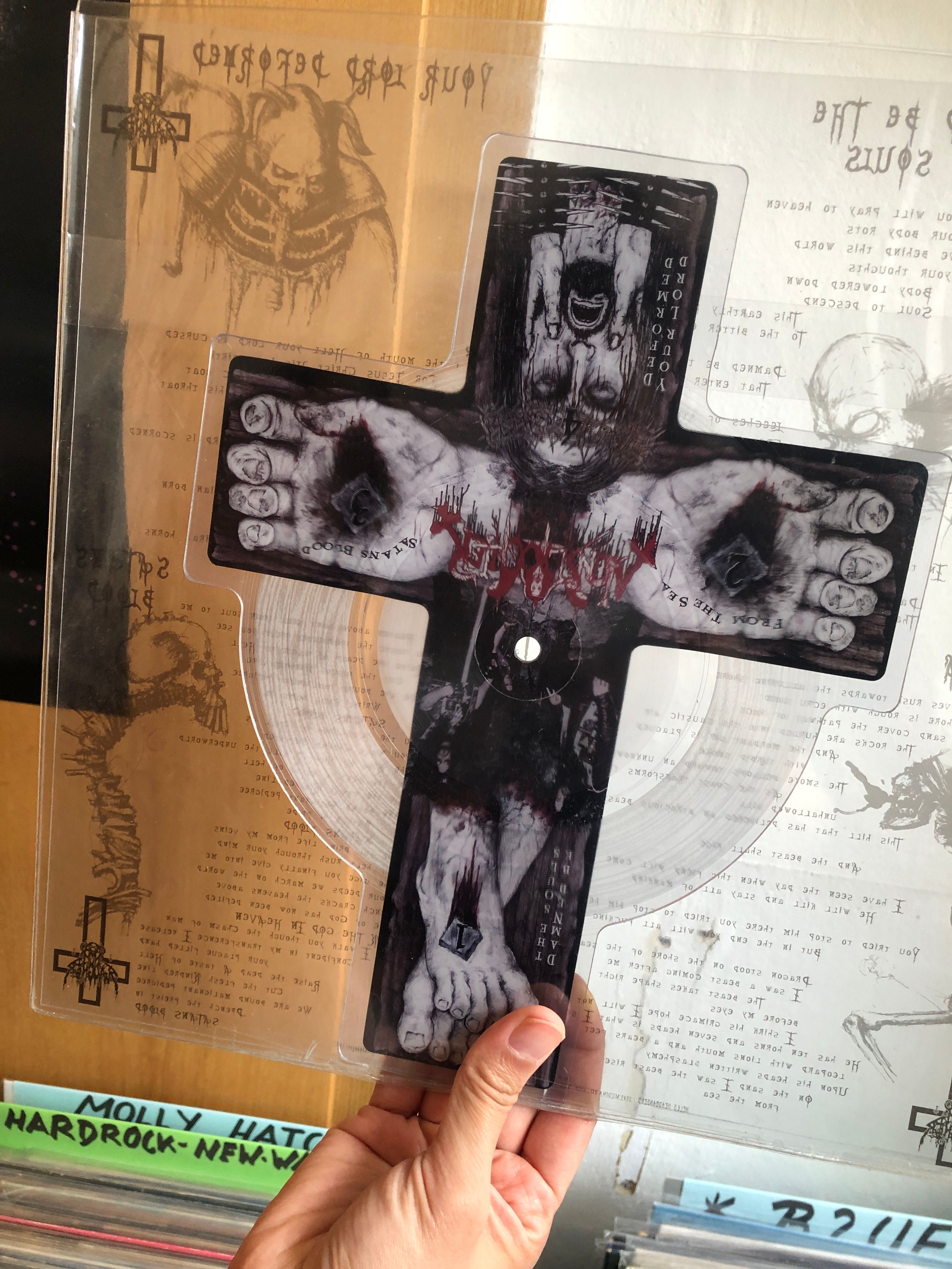 Hand holding a clear cross-shaped picture-disc vinyl printed with grisly crucifixion art