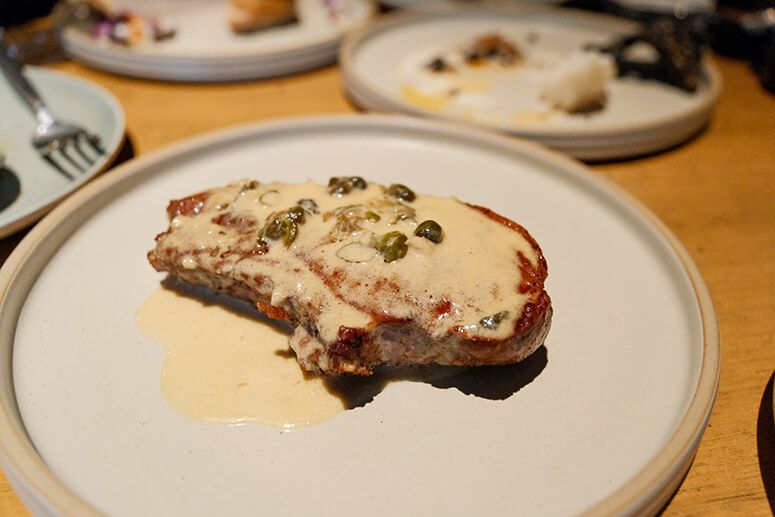 Berkshire pork chop draped in mustard cream sauce studded with capers, on a stone-gray plate