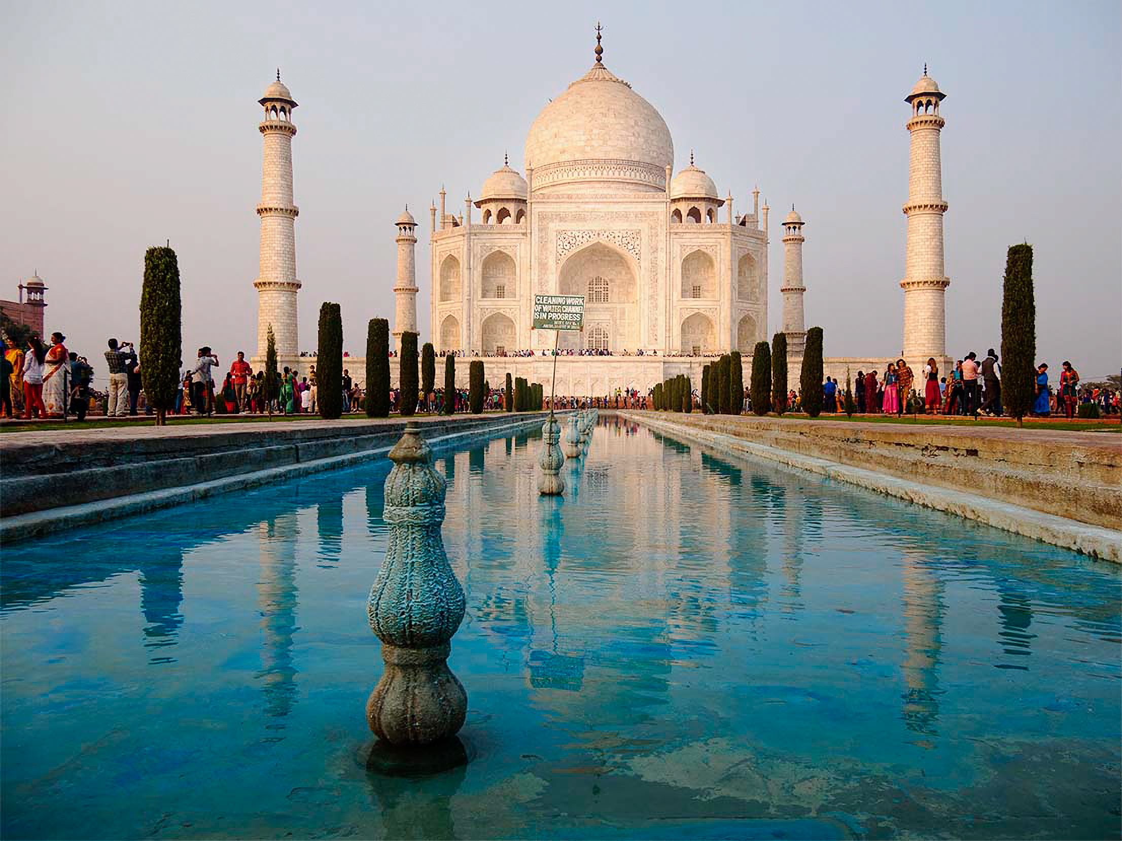 The Taj Mahal at dusk, its white dome mirrored in a long reflecting pool lined with visitors