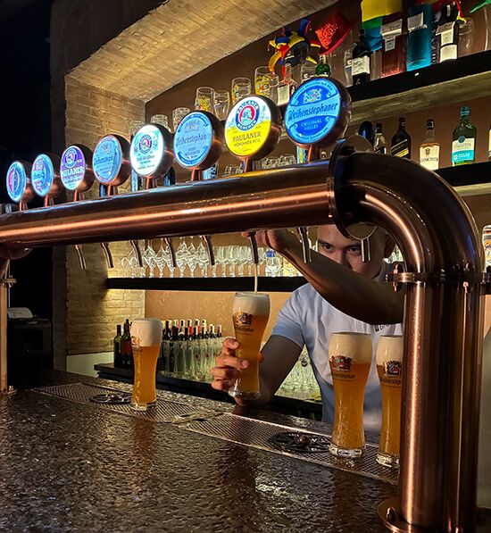 A bartender pours wheat beer from a copper tap tower lined with German beer badges at Brotzeit