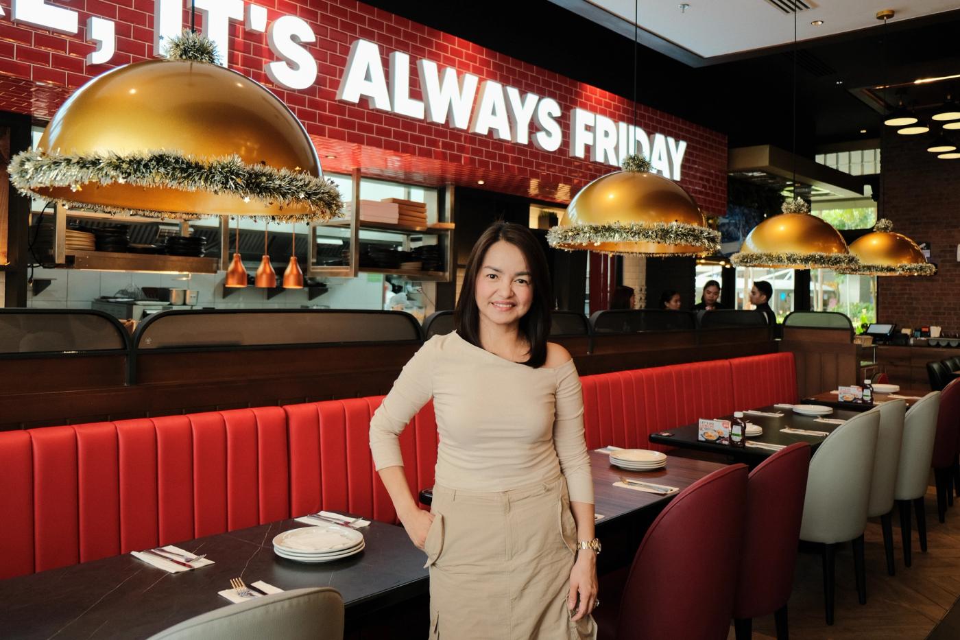 Rechelle Tiongson standing by red booths under gold dome lamps and the Always Friday sign