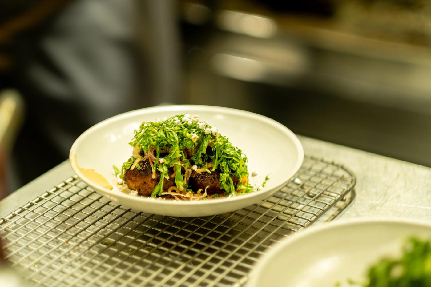 Meatballs piled with fresh arugula in a white bowl resting on a kitchen wire rack