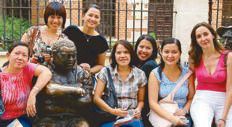 A group of women posing with a bronze seated statue in a courtyard in Alcalá de Henares