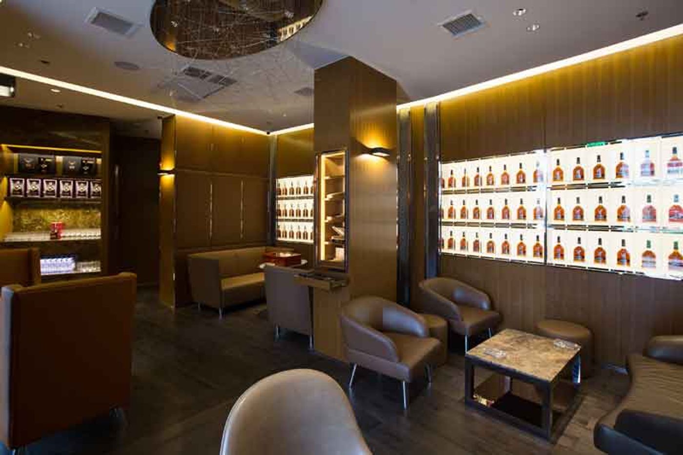 The Dalmore Cigar Lounge, with tan leather armchairs, a backlit wall of whisky bottles and a glass-fronted humidor under warm amber light
