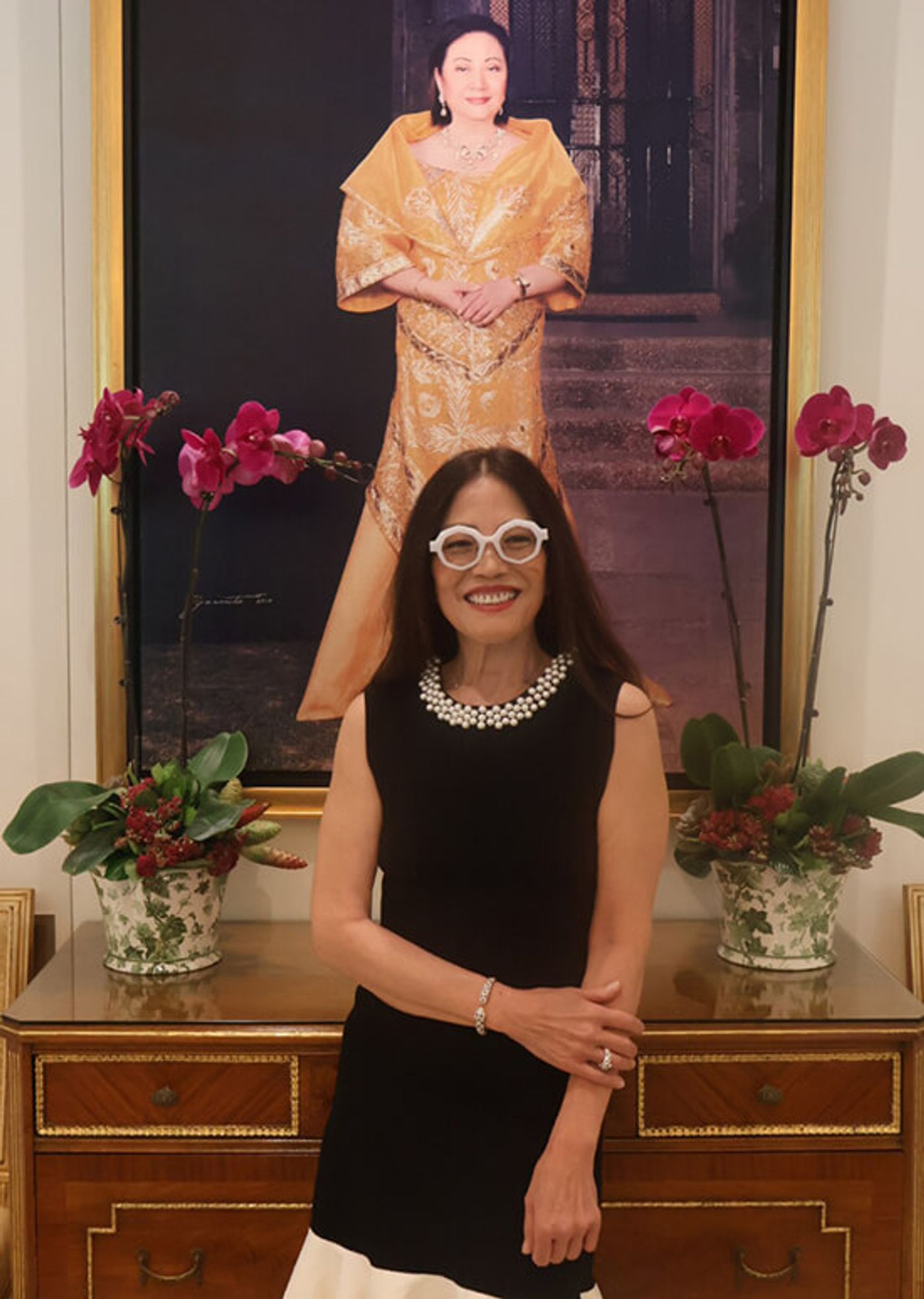 Cecile Licad in black stands before a portrait of Nedy Tantoco in a golden gown, flanked by orchids