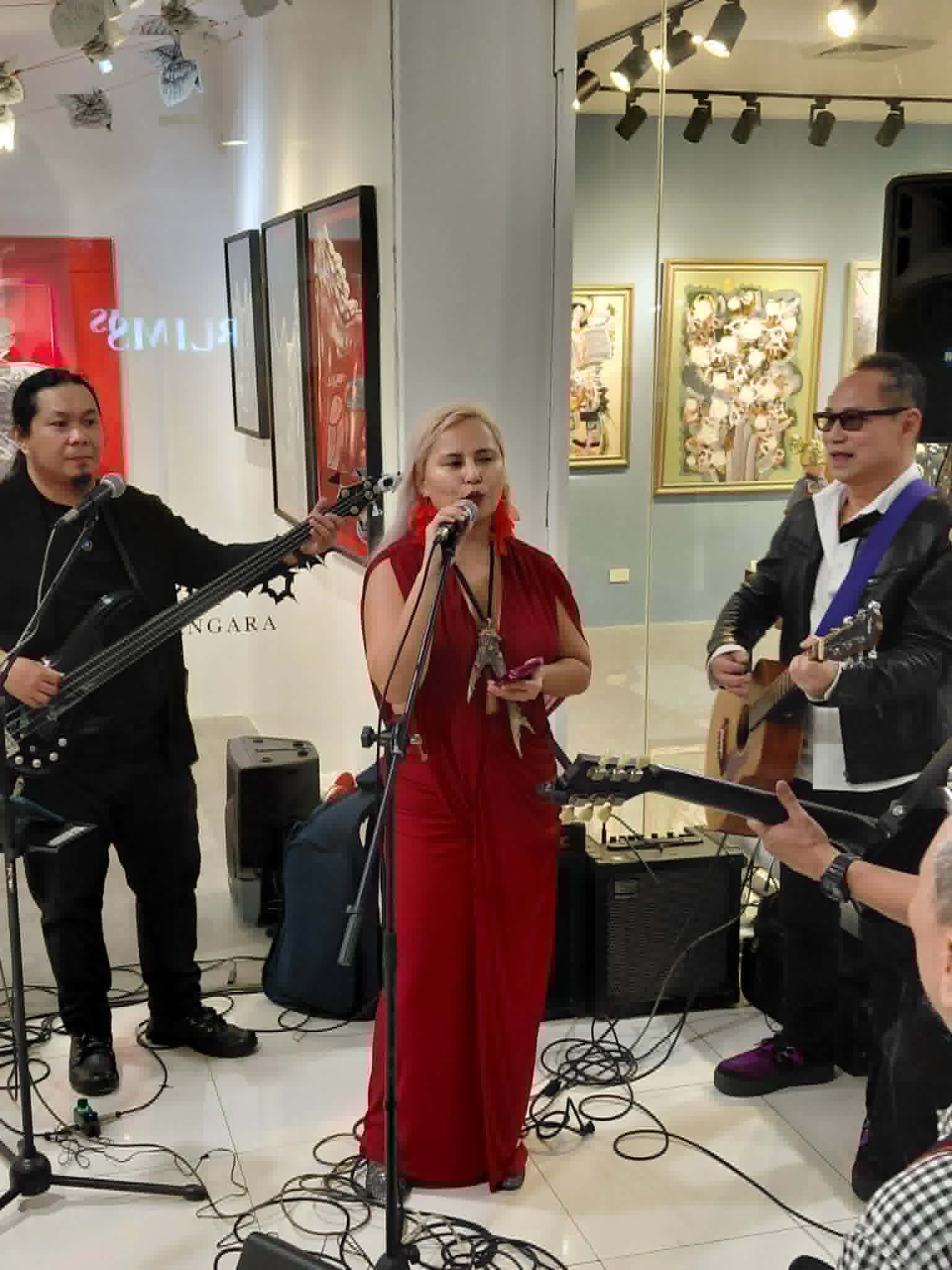 Katya Angara in a red dress singing at a microphone with Stephen Lu and band at the opening of Sorceress