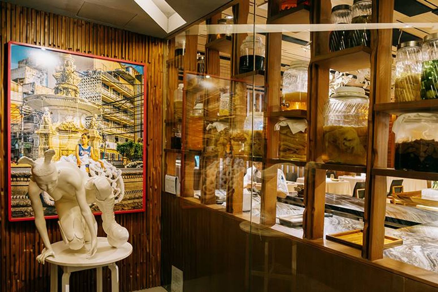 A white crouching sculpture and a framed photograph stand beside wooden shelves of fermentation jars in the gallery corner of Chef Chele Gonzalez’s restaurant