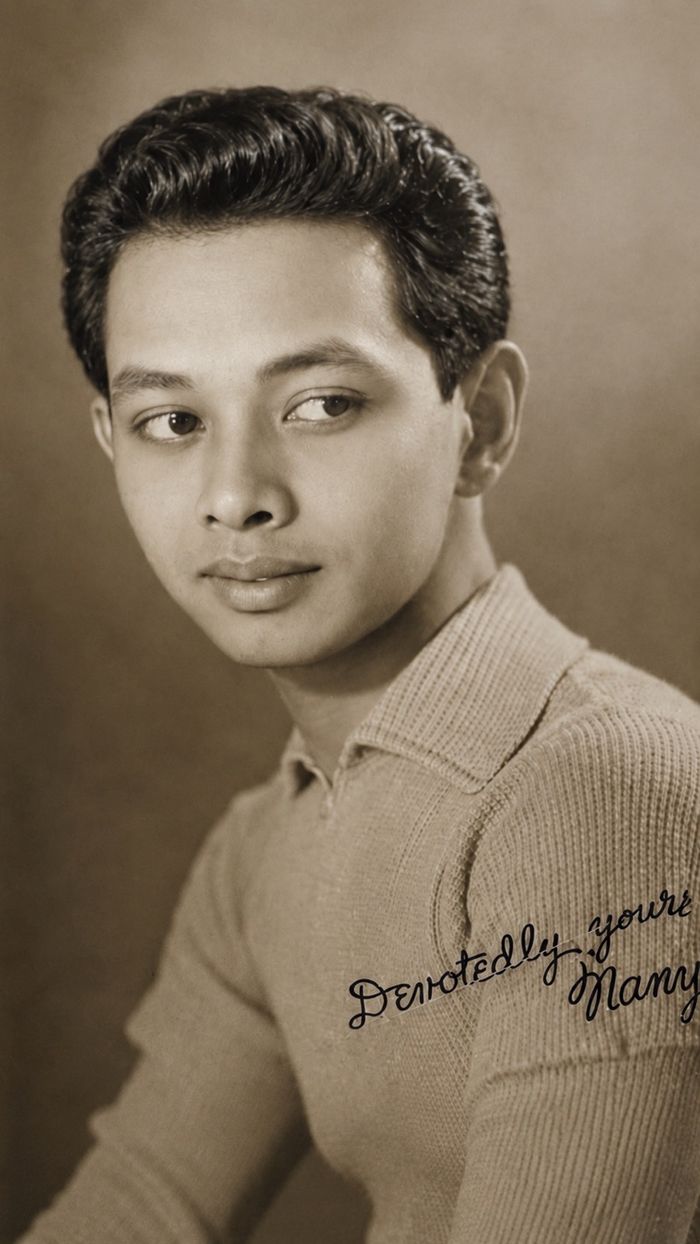 Sepia-toned vintage studio portrait of a young man with wavy hair in a knit collared shirt, a handwritten inscription reading ‘Devotedly yours’ across the shoulder