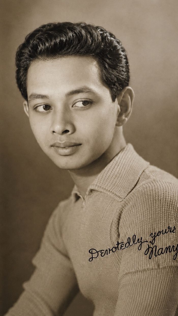 Sepia-toned vintage studio portrait of a young man with wavy hair in a knit collared shirt, a handwritten inscription reading ‘Devotedly yours’ across the shoulder