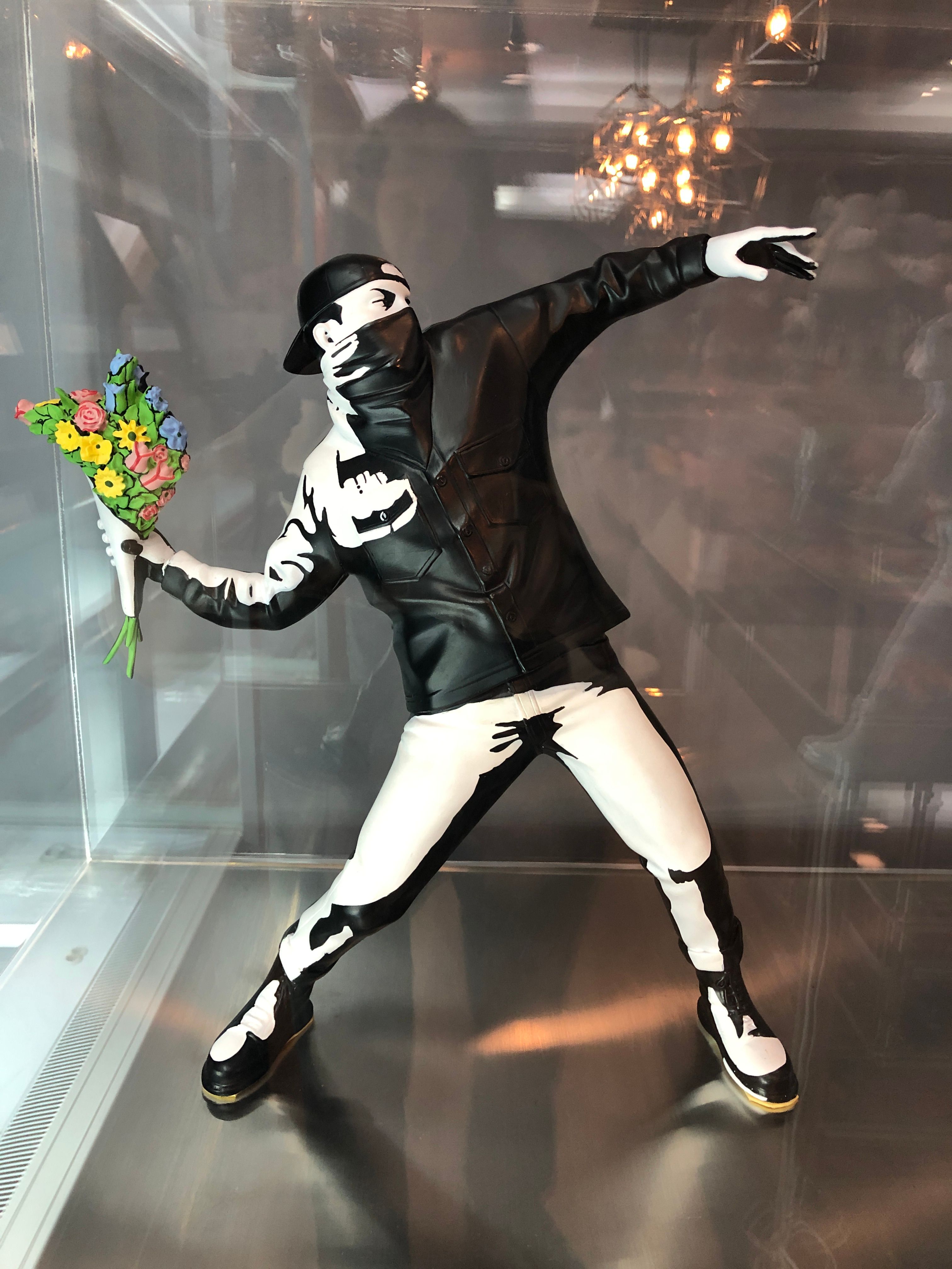 A figure of Banksy’s Flower Thrower in a display case, the masked man in a cap winding up to hurl a bouquet