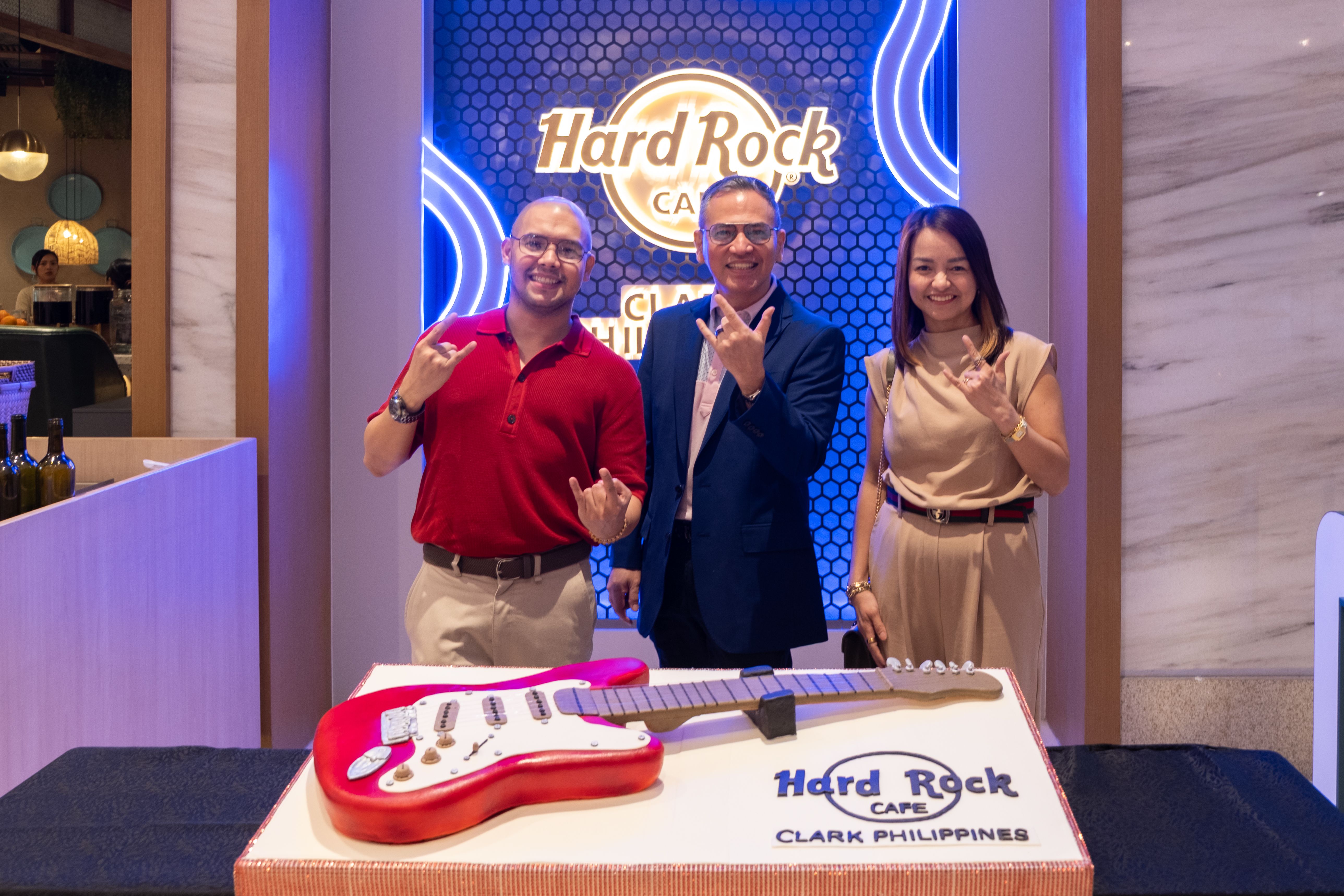 Three guests flash rock hand signs behind the guitar cake at Hard Rock Cafe Clark
