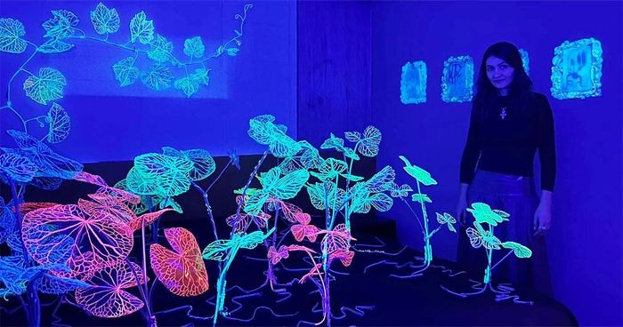 Andreea Medar stands among glowing wire plants in a room bathed in ultraviolet blue light