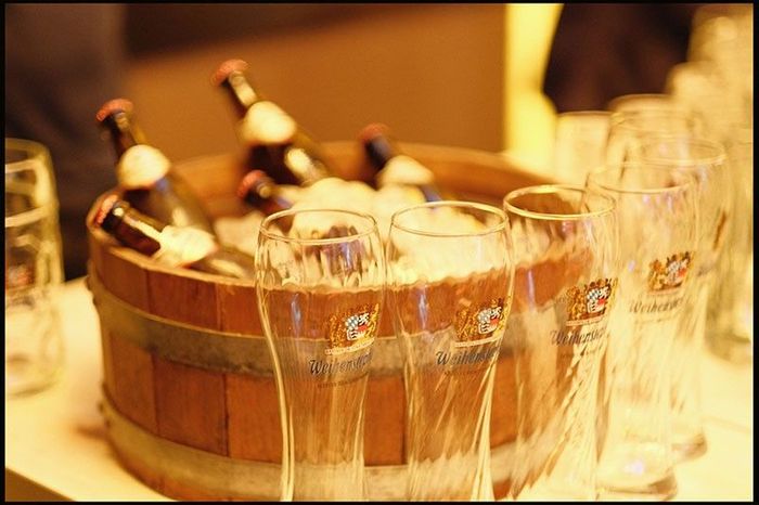 Weihenstephan beer bottles chilling in an ice-filled wooden tub, ringed by empty branded wheat-beer glasses