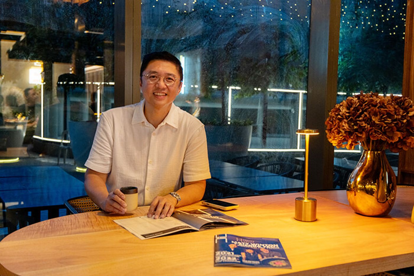 H Proper Coffee Roasters founder Harley Keith Yu seated at a wooden table with a cup of coffee