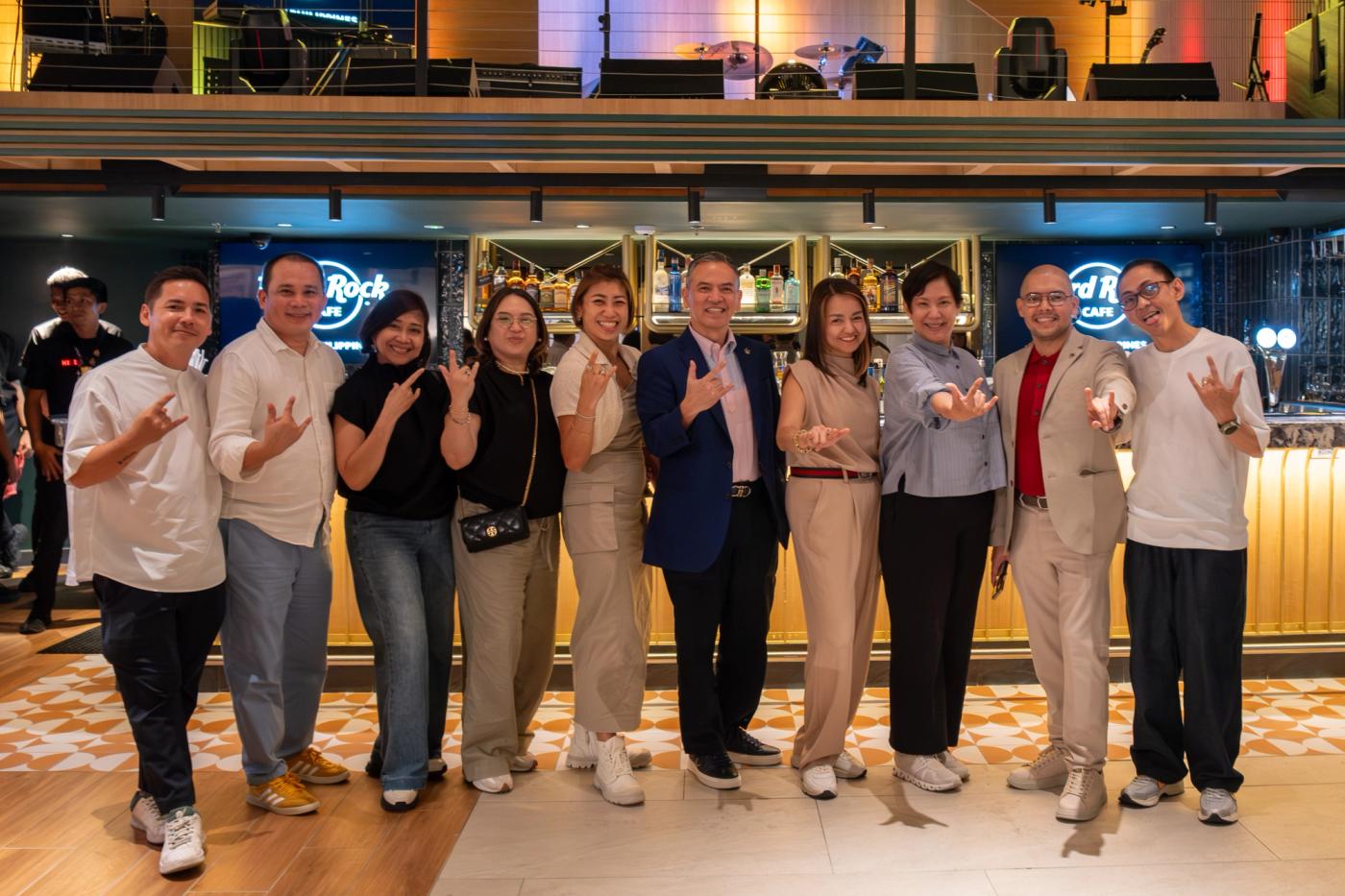 Bistro Group executives line up flashing rock hand signs in front of the cafe’s bar
