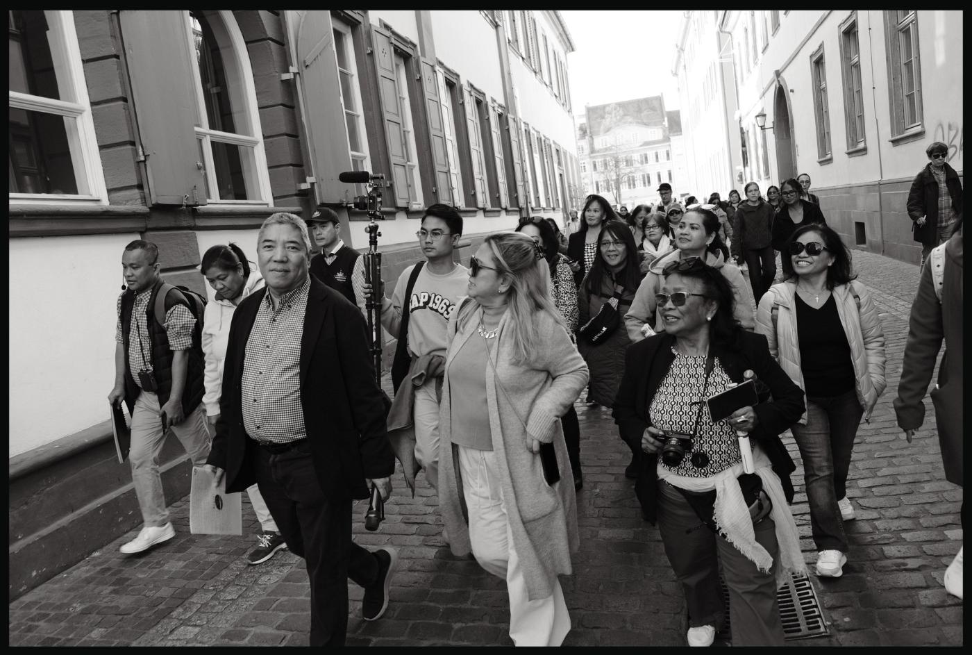 Historian Ambeth Ocampo leads a walking tour group down a cobbled Heidelberg street, in black and white
