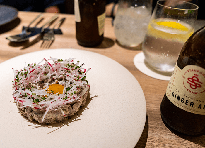 Ring of beef tartare crowned with an egg yolk and shaved radish, a bottle of ginger ale alongside