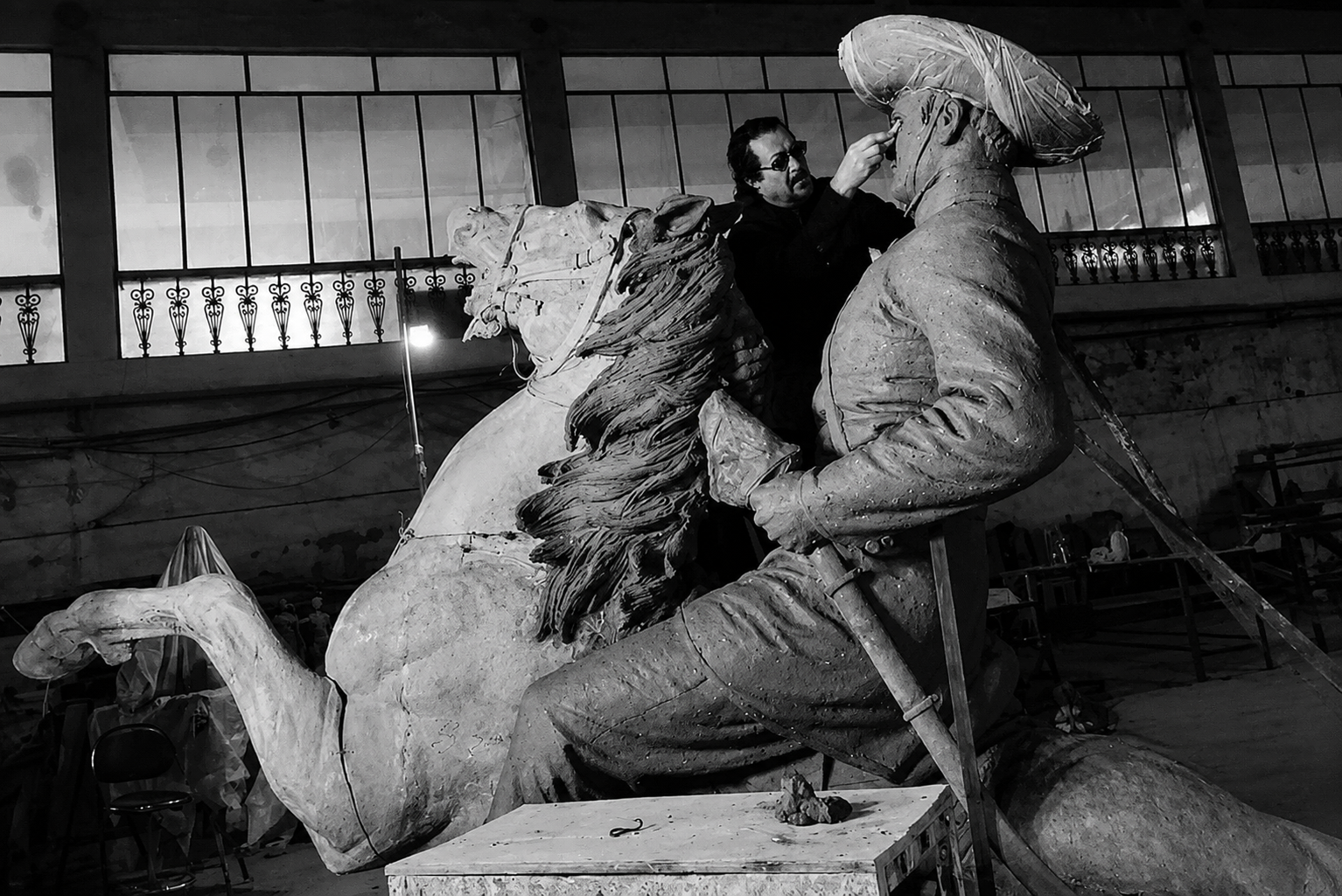 Spanish artist Ginés Serrán works on the face of his full scale clay model of General Martín Delgado on horseback, later cast in bronze for Iloilo, in a studio with tall windows
