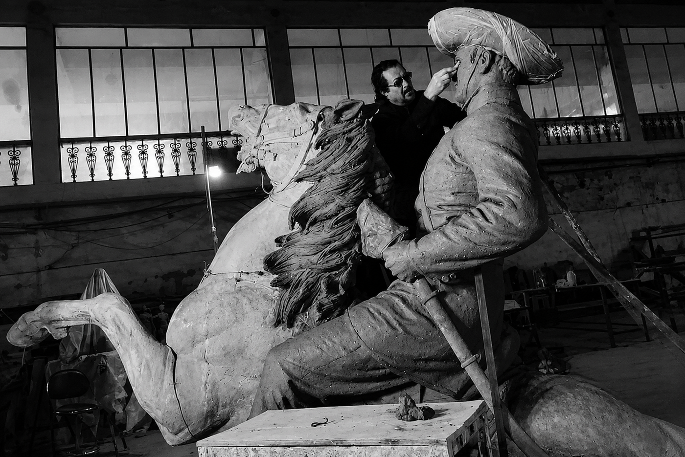 Spanish artist Ginés Serrán works on the face of his full scale clay model of General Martín Delgado on horseback, later cast in bronze for Iloilo, in a studio with tall windows