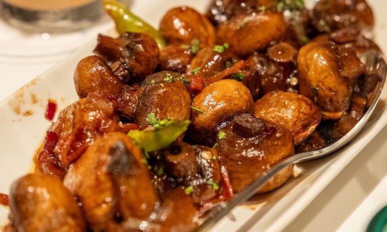 Platter of glossy sauteed mushrooms with chorizo bits, parsley and slivers of green chili