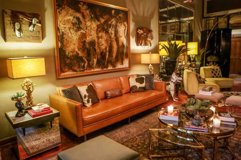 The Franciscos’ layered living room, a caramel leather sofa with cowhide pillows beneath a large earth-toned abstract painting and brass lamps