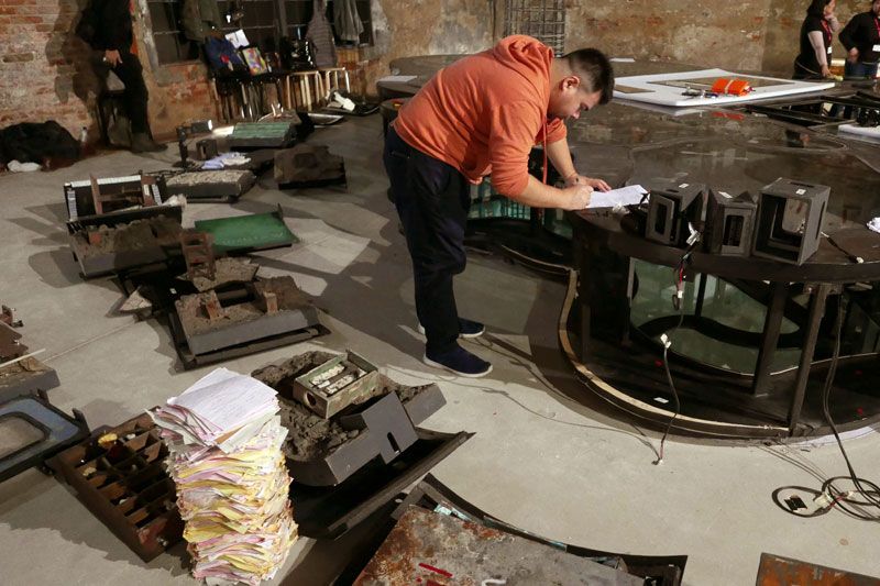 A worker in an orange hoodie checking paperwork over the disassembled sections of Island Weather