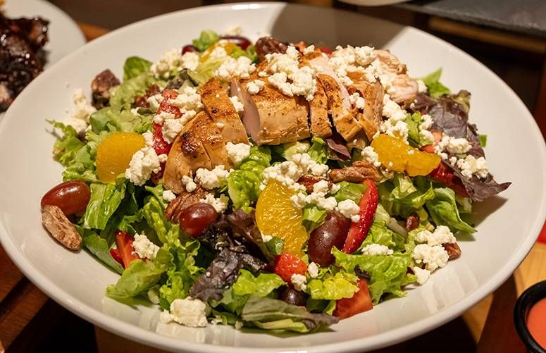 Grilled chicken and strawberry salad topped with crumbled cheese, orange segments and grapes
