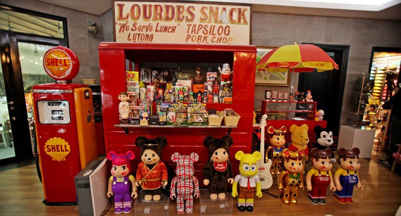 A restored red Shell petrol pump and an old Lourdes Snack karinderia sign above a row of Bearbricks in Japanese and cartoon liveries