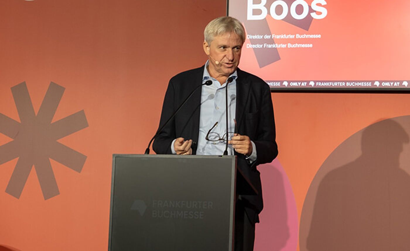 Frankfurter Buchmesse director Juergen Boos speaking at a lectern in front of a red backdrop