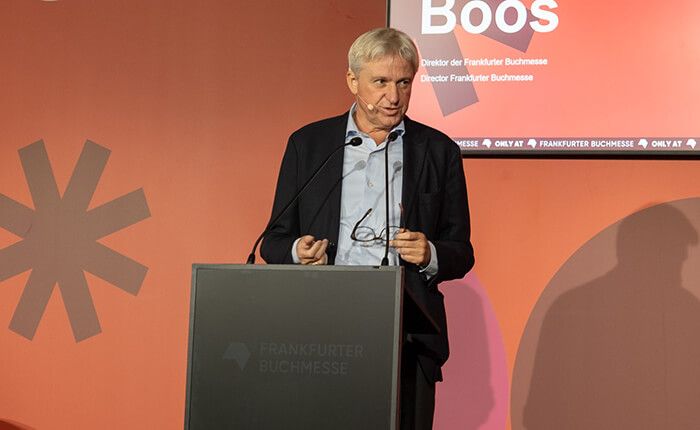Frankfurter Buchmesse director Juergen Boos speaking at a lectern in front of a red backdrop