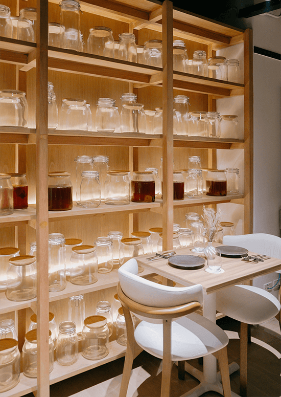 Backlit wooden shelves lined with glass infusion jars behind a set table at Juniper