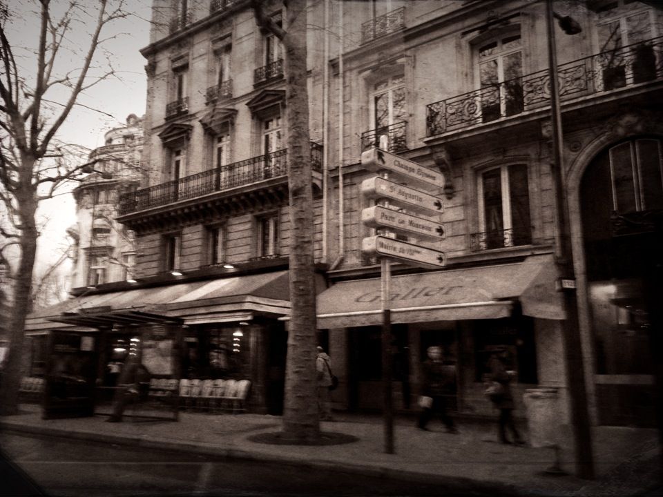 Sepia street scene of Parisian cafe awnings and balconied facades, pedestrians passing a signpost