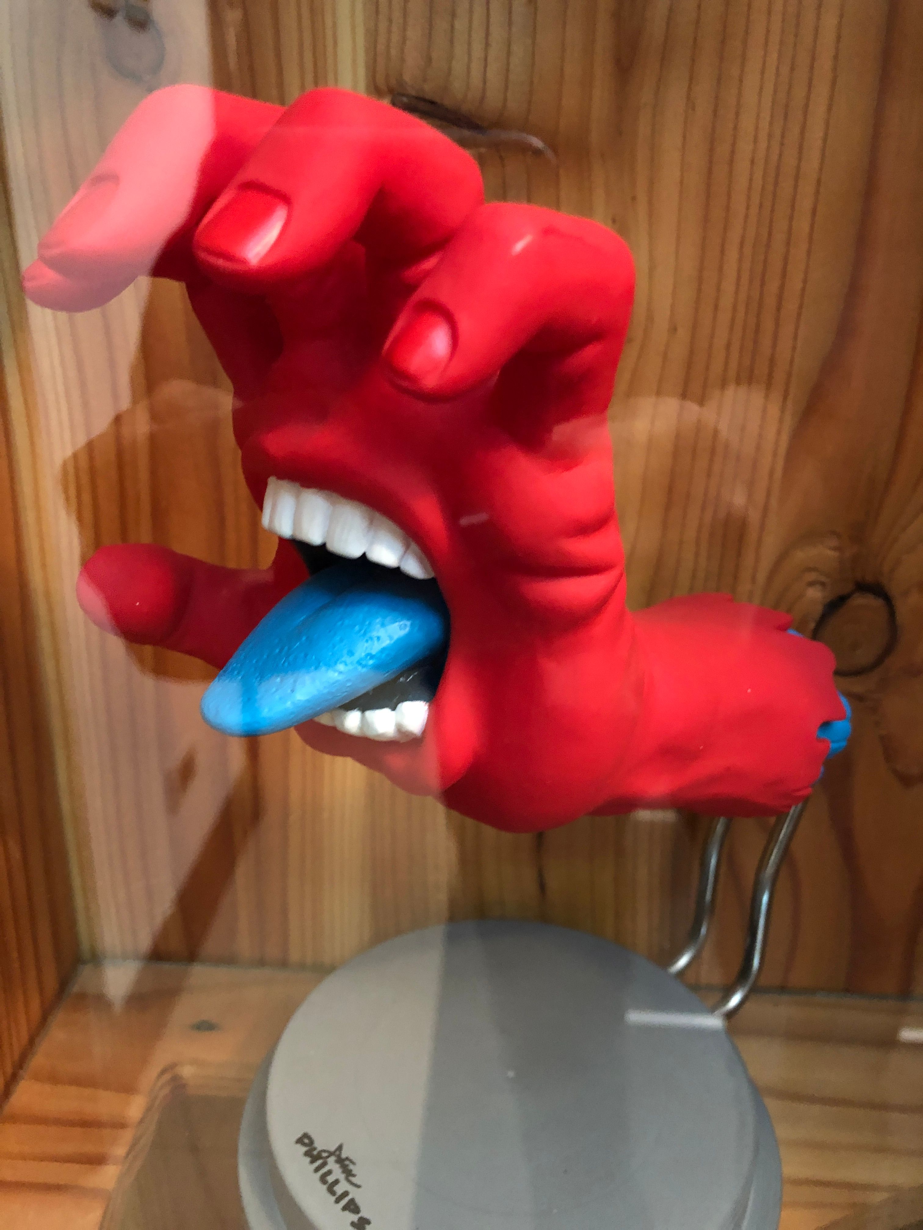 Jim Phillips’ Screaming Hand as a figure, a red hand with bared teeth and a blue tongue mounted on a stand against pine boards